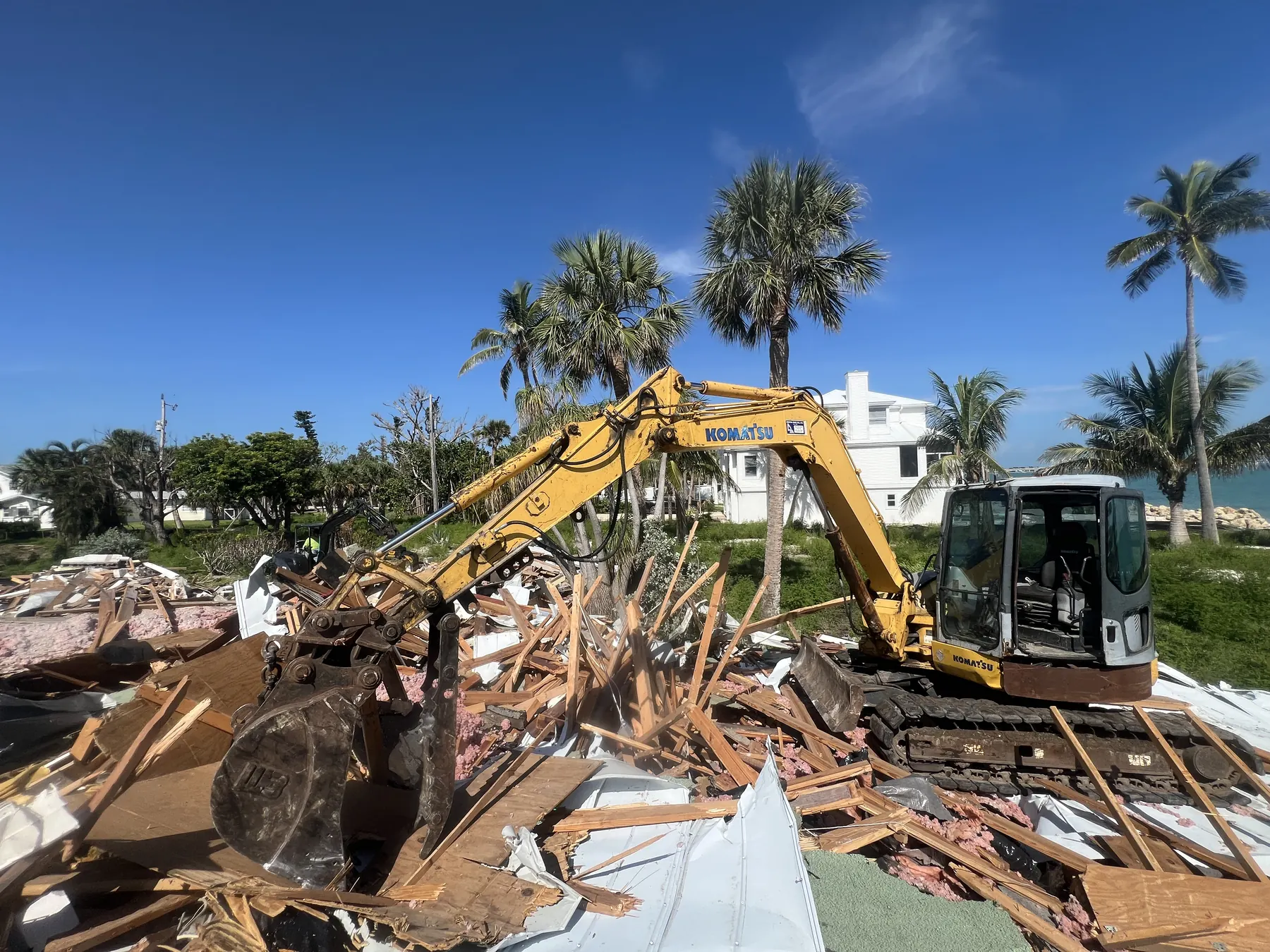 Excavator clearing demolition debris from a palm-lined property